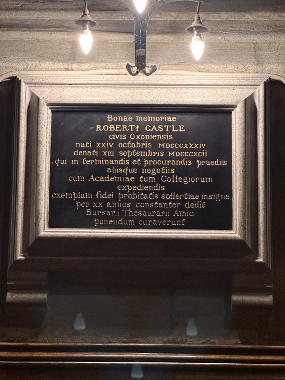 Latin memorial to Robert Castle, with gold lettering on a black panel in a stone frame.